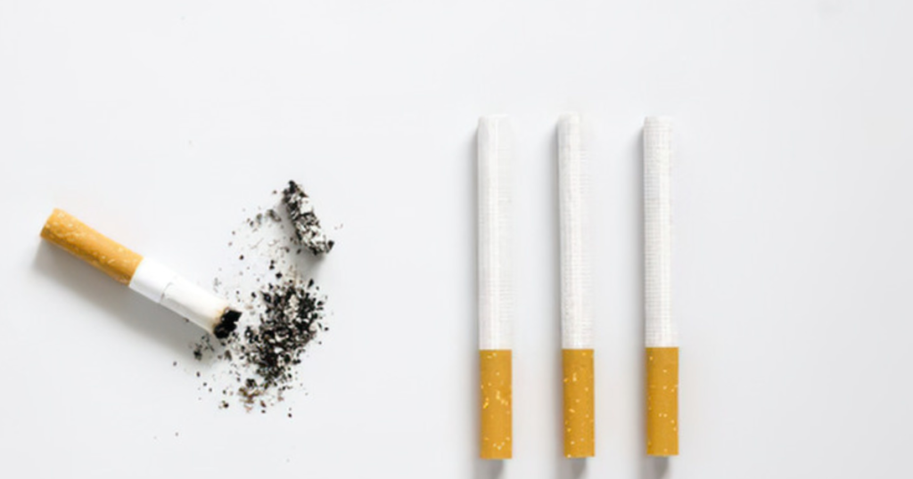 Um cigarro apagado ao lado de três cigarros intactos sobre uma superfície branca, representando o ato de parar um hábito ruim